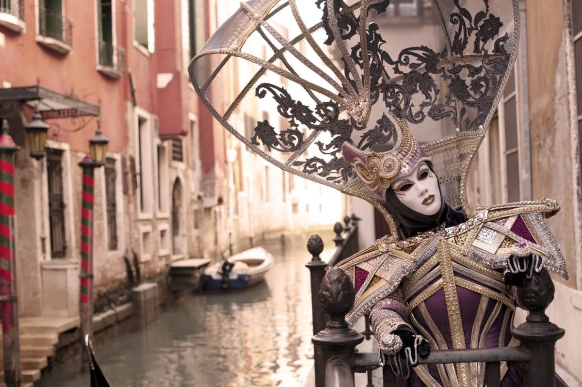 Attractive masked person posing in front of house building at one of numbered canals in Venice, Italy.